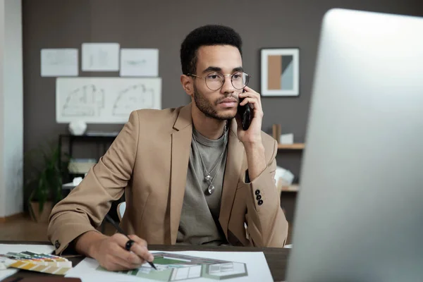 Jeune designer sérieux avec smartphone par l'oreille en regardant l'écran d'ordinateur — Photo