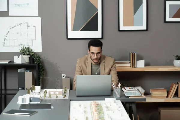 Young serious biracial businessman looking at laptop screen while sitting by table — Fotografia de Stock