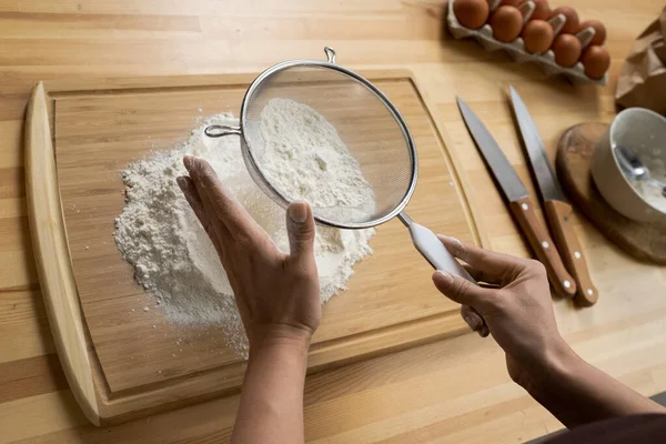 Mãos de chef feminino peneirando farinha sobre tábua de corte — Fotografia de Stock