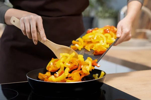 Hands of young woman putting chopped yellow pepper in frying pan — ストック写真