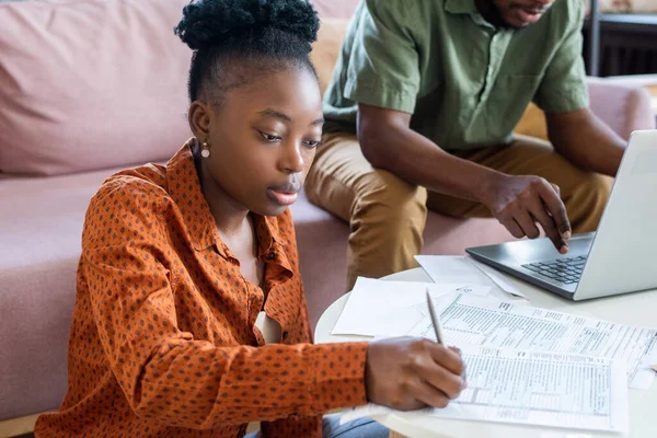 Jeune femme africaine sérieuse prenant des notes dans le document financier — Photo