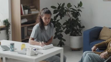 Genç bayan doktorun randevu sırasında tekerlekli sandalyedeki yaşlı kadını dinlerken not aldığı orta boy PAN fotoğrafı.