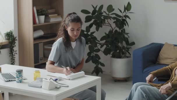 Medium Pan Shot Young Female Doctor Taking Notes Clipboard While — Stockvideo