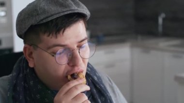 Güneş gözlüğü takan, şapkalı, kurabiye yiyen ve gündüz vakti mutfakta kameraya gülümseyen şık beyaz adamın göğsü.