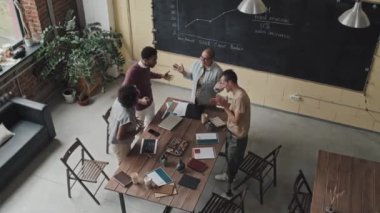 Gündüz vakti modern ofisteki konferans masasının etrafında duran dört kadın ve erkek iş arkadaşının yüksek açılı görüntüsü. Finansal projeyi bitirdikten sonra ekip olarak konuşup el ele tutuşuyorlar.