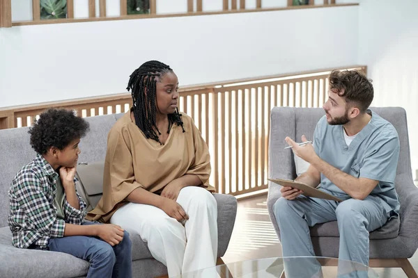 Jeune dentiste confiant donnant consultation à une jeune femme africaine avec son fils — Photo