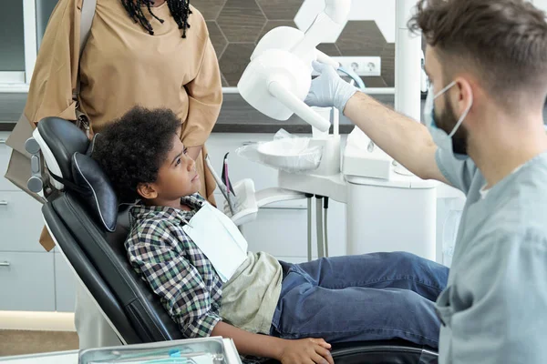 歯医者の椅子に座っている間に医療用ランプを見ている小さなアフリカの少年 — ストック写真