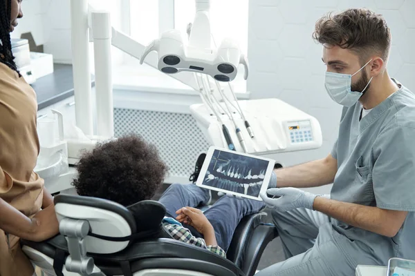 Стоматолог в захисному одязі, що показує рентген щелепи маленькому пацієнту — стокове фото