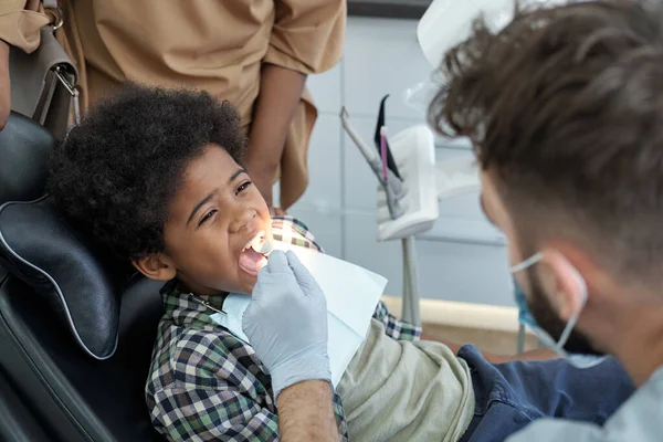 Little boy with open mouth having oral check-up while sitting in armchair — Stock Photo, Image
