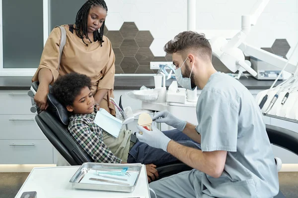 Contemporary stomatologist showing false teeth to little patient — Stock Photo, Image
