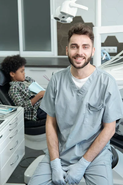 Jovem estomatologista feliz em luvas e uniforme olhando para você — Fotografia de Stock