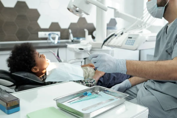 Glovoed hand of dentist holding mirror while sitting in front of boy — Stock Photo, Image