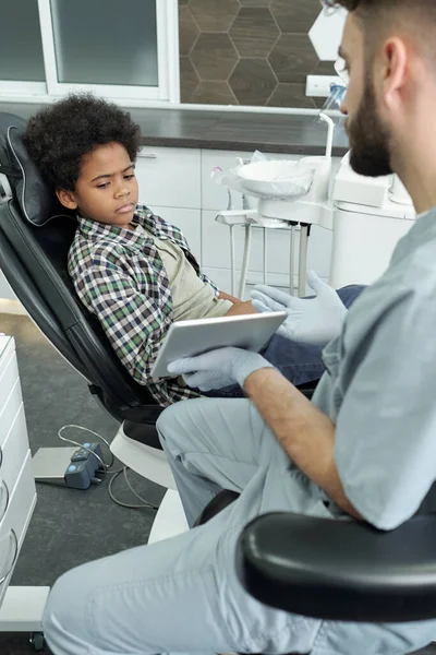 Lindo niño mirando la pantalla de la tableta sostenida por el dentista — Foto de Stock