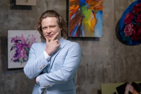 Reifer Künstler in blauer Jacke steht mit seinen Kunstwerken an der Wand — Stockfoto