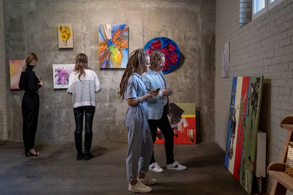 Várias visitantes femininas da galeria de arte olhando para pinturas — Fotografia de Stock