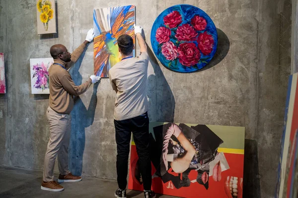 Dois jovens trabalhadores do sexo masculino da galeria de arte pendurado pinturas na parede — Fotografia de Stock