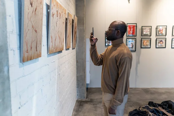 Jovem africano com smartphone tirando fotos da pintura no museu — Fotografia de Stock