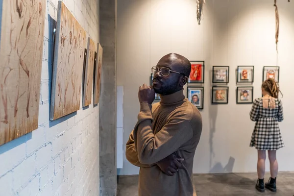 Homem africano sério em pulôver marrom olhando para a pintura — Fotografia de Stock