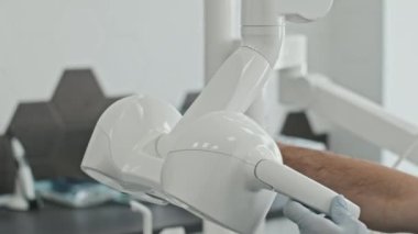 Kırpılmış erkek doktor eldiven takıyor. Parlak ofiste diş ameliyat lambasını ayarlıyor.