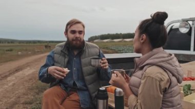 Yetişkin bir adam ve bir kadın pikapta rahat bir şekilde oturuyor ve çiftlik alanında öğle yemeği molası veriyorlar.