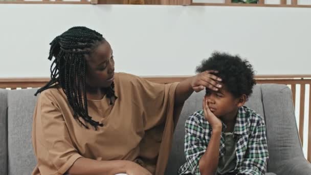 中等年龄的黑人妇女和她十岁的儿子坐在接待室的沙发上 母亲让牙痛的男孩平静下来 — 图库视频影像