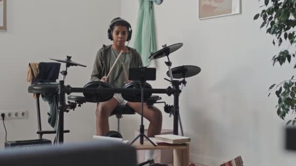 明るい11歳のアフリカ系アメリカ人の少女の中長い耳の上のヘッドフォンを身に着けています 電子ドラムを再生します — ストック動画