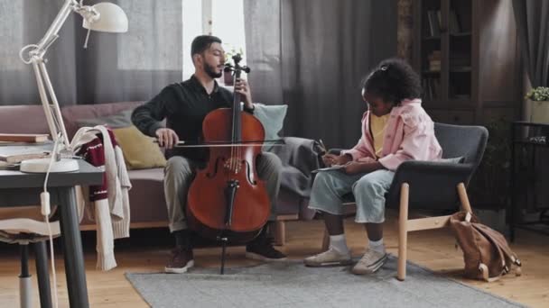 곱슬머리 노트를 아시아 음악가가 베이스를 연주하는 집에서 소파에 — 비디오