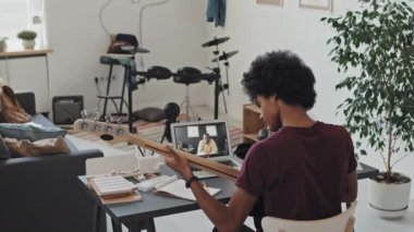 Elektro gitar çalan genç bir adamın gündüz vakti odada oturması, erkek siyahi müzik öğretmenini dizüstü bilgisayardan araması.