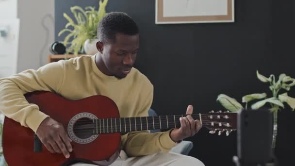 Médium Jovem Negro Sentado Poltrona Casa Durante Dia Tocando Guitarra — Vídeo de Stock
