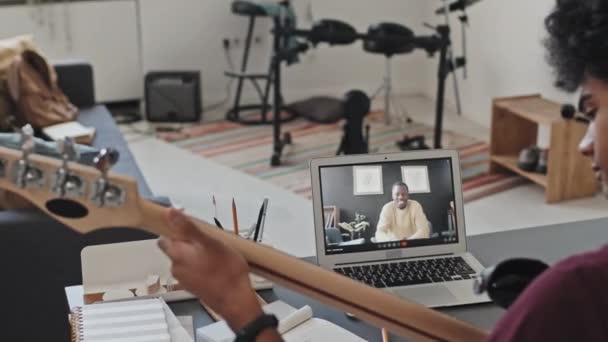 坐在办公桌前弹奏电吉他的年轻人肩并肩地坐在房间里 视频通过笔记本电脑给黑人男性音乐老师打电话 — 图库视频影像