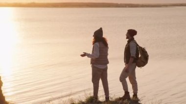 Yavaş çekim, uçurumun kenarındaki genç adam ve kadının inanılmaz günbatımı manzarasına hayran kaldıkları uzun çekim görüntüleri.