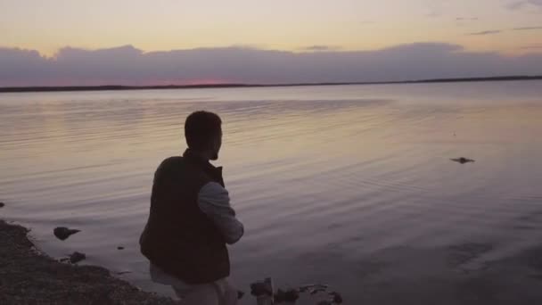 水平中出しの認識できない若い男支出夜オン湖畔遊び石スキップ — ストック動画