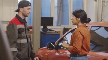 Üniformalı profesyonel bir tamirci kadın müşteriye araba anahtarı veriyor ve otoparkta onunla konuşuyor.