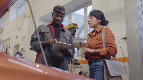 非洲裔美国人汽车修理工和西班牙裔女性顾客站在敞篷汽车旁 讨论数字平板电脑上的一些问题 — 图库视频影像