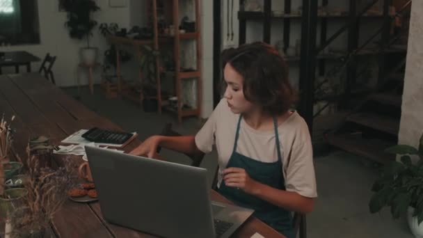 앞치마를 도자기 작업장에서 테이블에 휴대용 컴퓨터를 사용하고 전화를 머리를 여성의 — 비디오