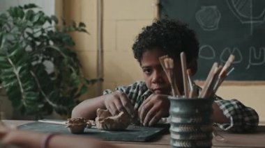 Çömlek atölyesinde masa başında oturan, kil şekillendiren, gün içinde seramik el sanatları yapan,