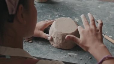 Küçük beyaz bir kızın omuzları üzerinde. Gündüz vakti masa başında oturuyor, kilden bir kase yapıyor, ahşap bir aletle kesiyor.