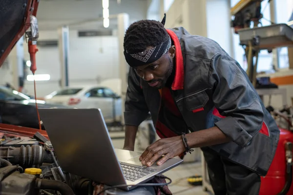 Young African repairman consulting websites while checking and repairing engine — Stock Photo, Image