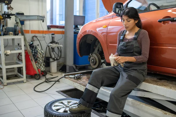 Jonge vermoeide vrouwelijke werknemer van de onderhoudsdienst voor auto 's die handschoenen uitdoet — Stockfoto