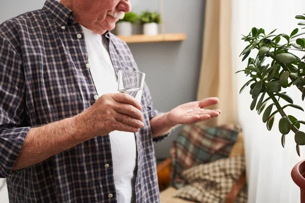 Manos de hombre mayor sosteniendo vaso de agua y píldora — Foto de Stock