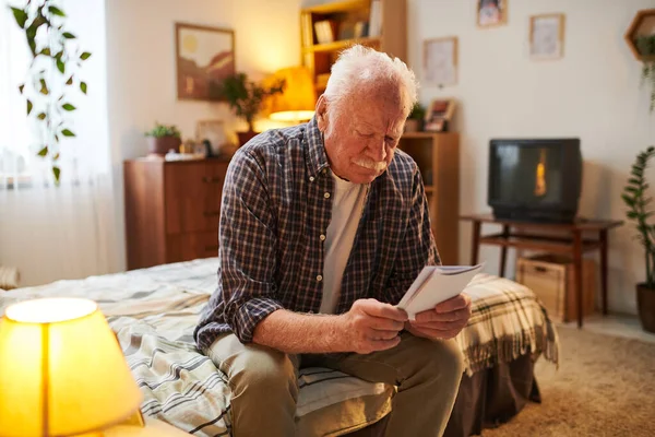 Uomo anziano contemporaneo guardando attraverso le fotografie dei suoi parenti — Foto Stock