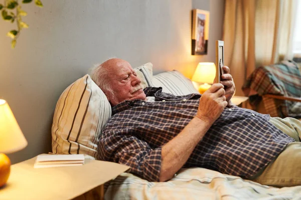 무심결에 침대에 누워 아내의 사진을 보고 있는 노인 — 스톡 사진