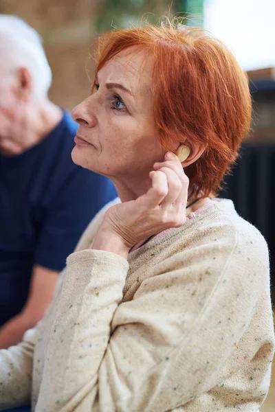 Ανώτερη γυναίκα με πουλόβερ που αγγίζει το αυτί της με ακουστικό βαρηκοΐας — Φωτογραφία Αρχείου