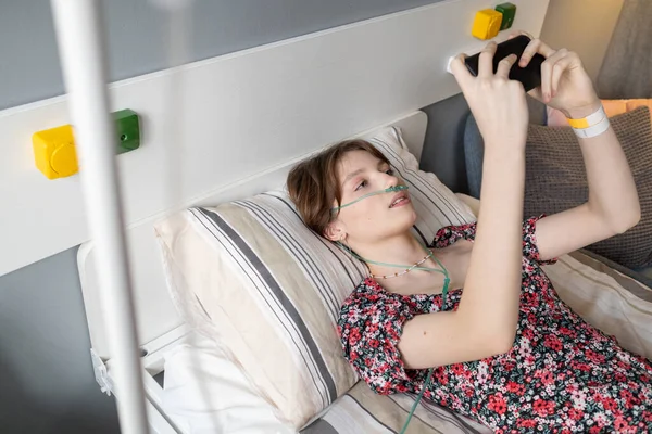 Chica enferma jugando en el teléfono móvil en la sala —  Fotos de Stock