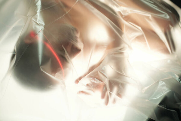 Young female cyberpunk covered with cellophane lying on table