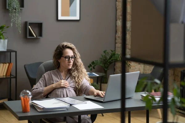 Joven mujer de negocios embarazada sosteniendo la mano sobre su vientre mientras hace networking — Foto de Stock