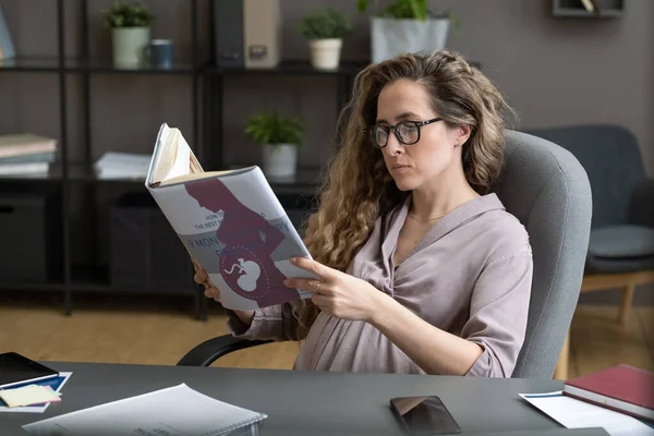 Joven mujer de negocios embarazada leyendo libro sobre el embarazo y el parto — Foto de Stock
