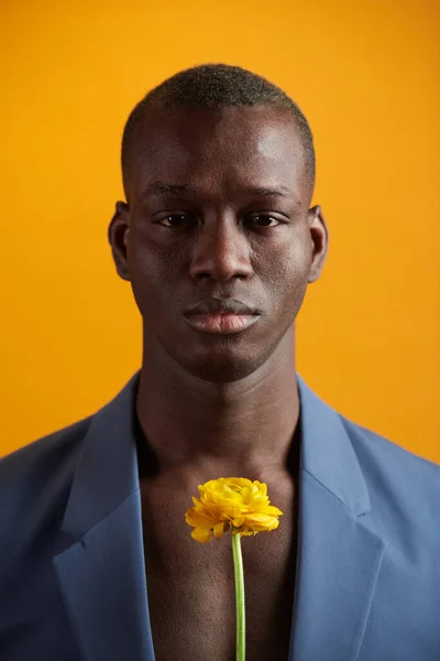 Poważny młody człowiek w niebieskiej kurtce na swoim ciele bez koszuli trzymając żółty kwiat — Zdjęcie stockowe