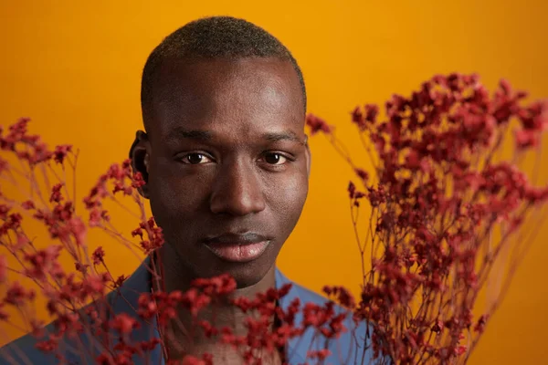 Twarz młodego Afrykanina otoczonego czerwonymi kwiatami — Zdjęcie stockowe