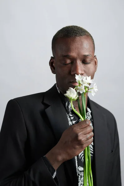 Elegante joven con chaqueta y camisa oliendo flores — Foto de Stock